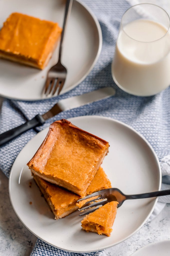 Pumpkin gooey butter cake on white plates, next to a glass of milk