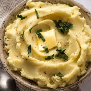 creamy mashed potatoes in a bowl topped with butter and parsley