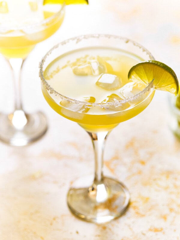 a beer margarita in a coupe glass with a salt rim and a lime wedge.