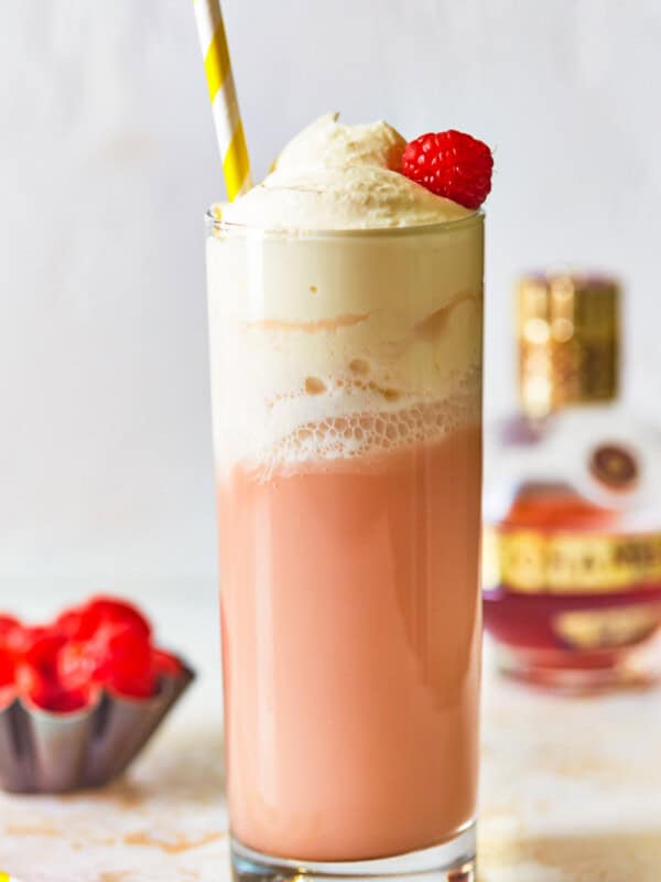 side view of raspberry italian cream soda in a tall glass topped with whipped cream, a raspberry, and a straw.