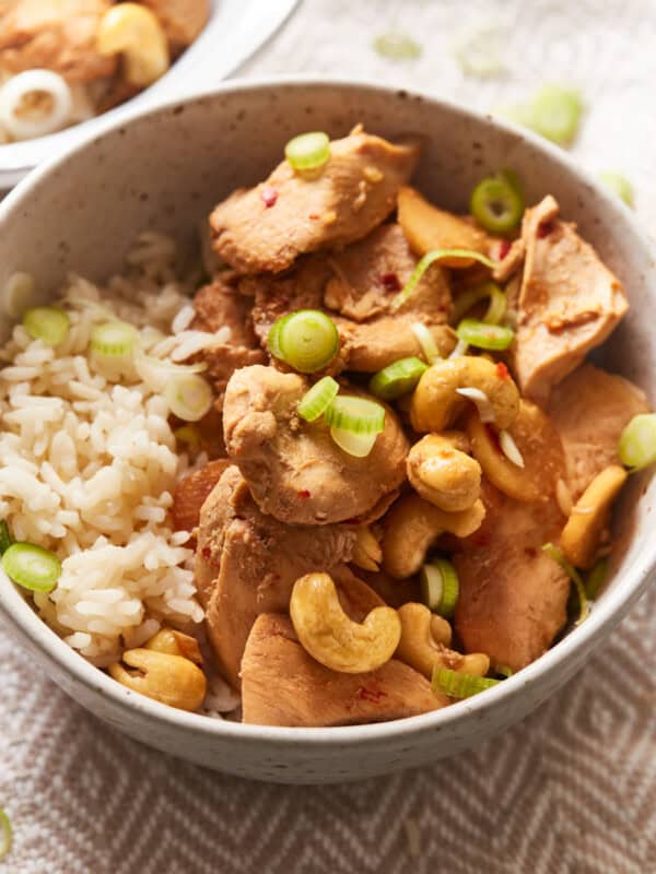 three-quarters view of crockpot cashew chicken in a tan bowl with rice.