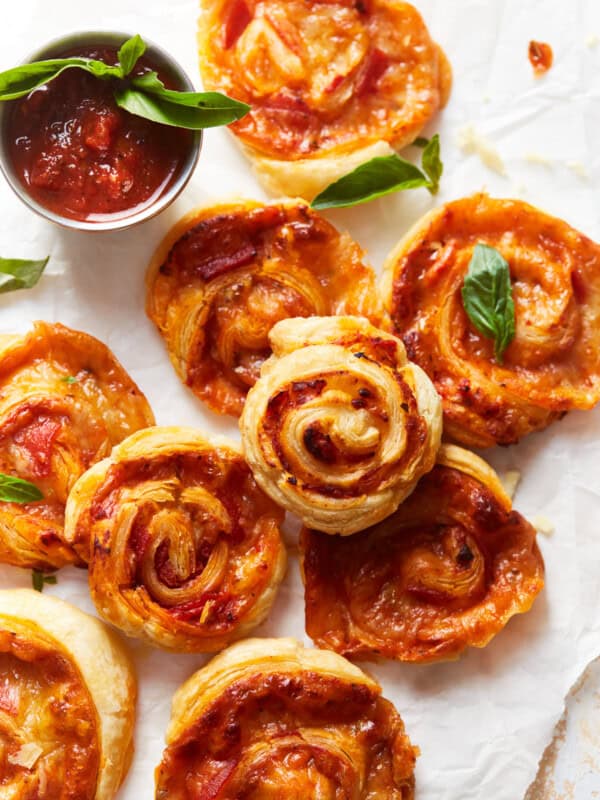 overhead view of pepperoni pizza rolls on parchment paper next to a small cup of marinara sauce.