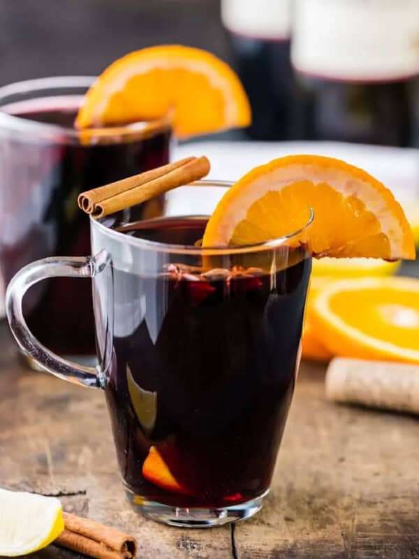 Two glasses of glühwein with orange slices and cinnamon sticks.