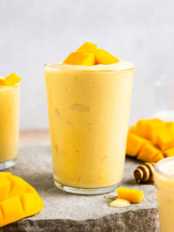 side view of a mango smoothie in a glass with mango chunks on top.