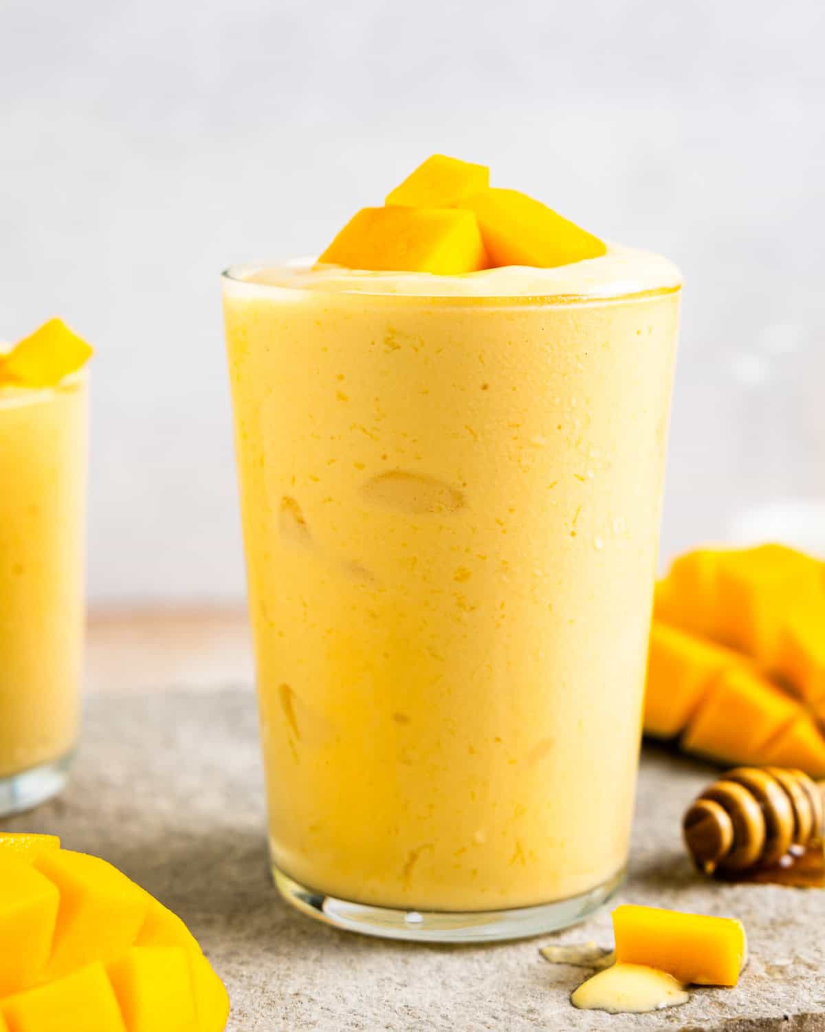 side view of a mango smoothie in a glass with mango chunks on top.