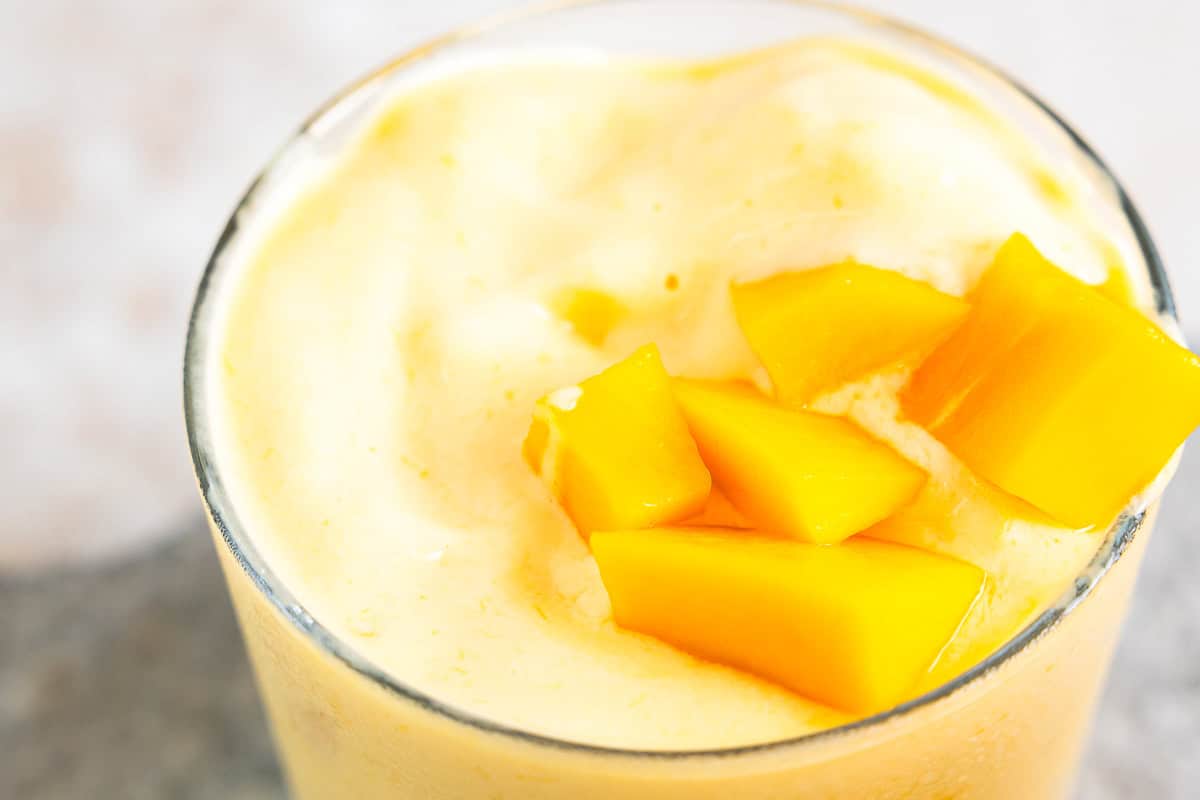 closeup of a mango smoothie in a glass topped with mango chunks.