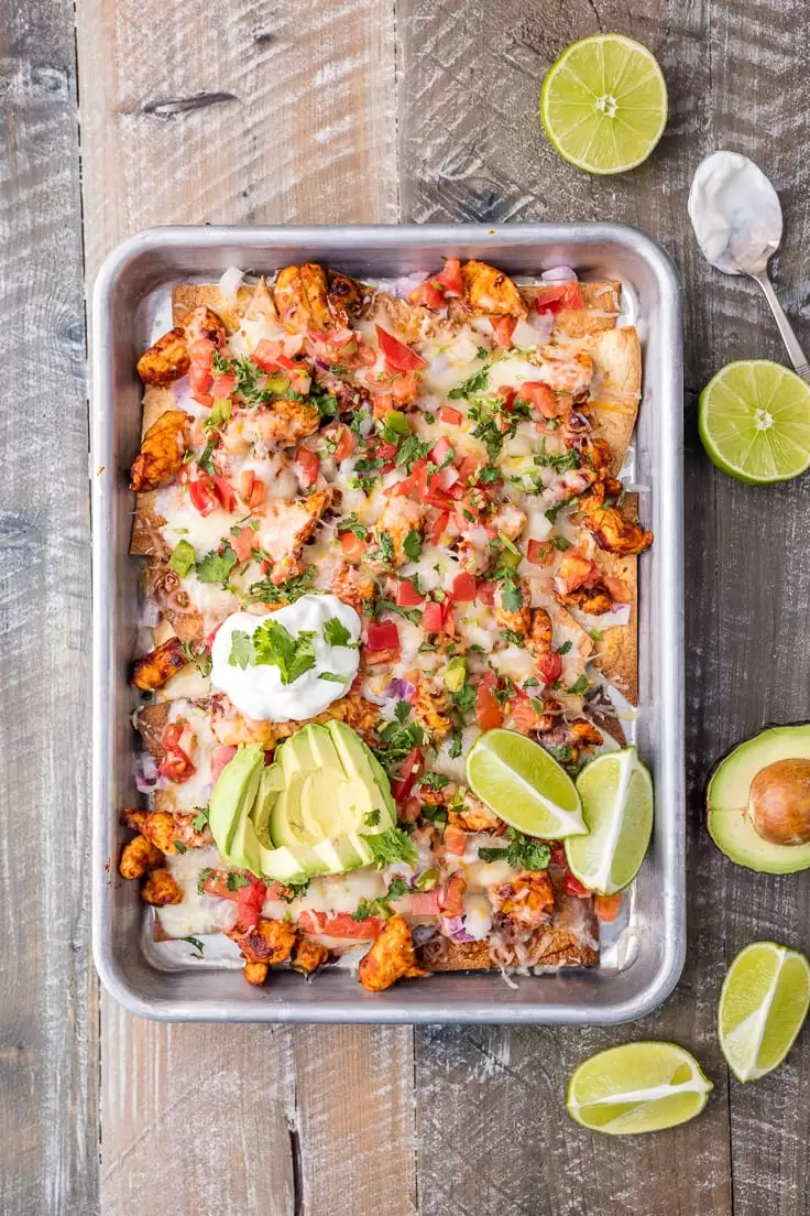 a sheet pan filled with chicken nachos on a wooden table surface