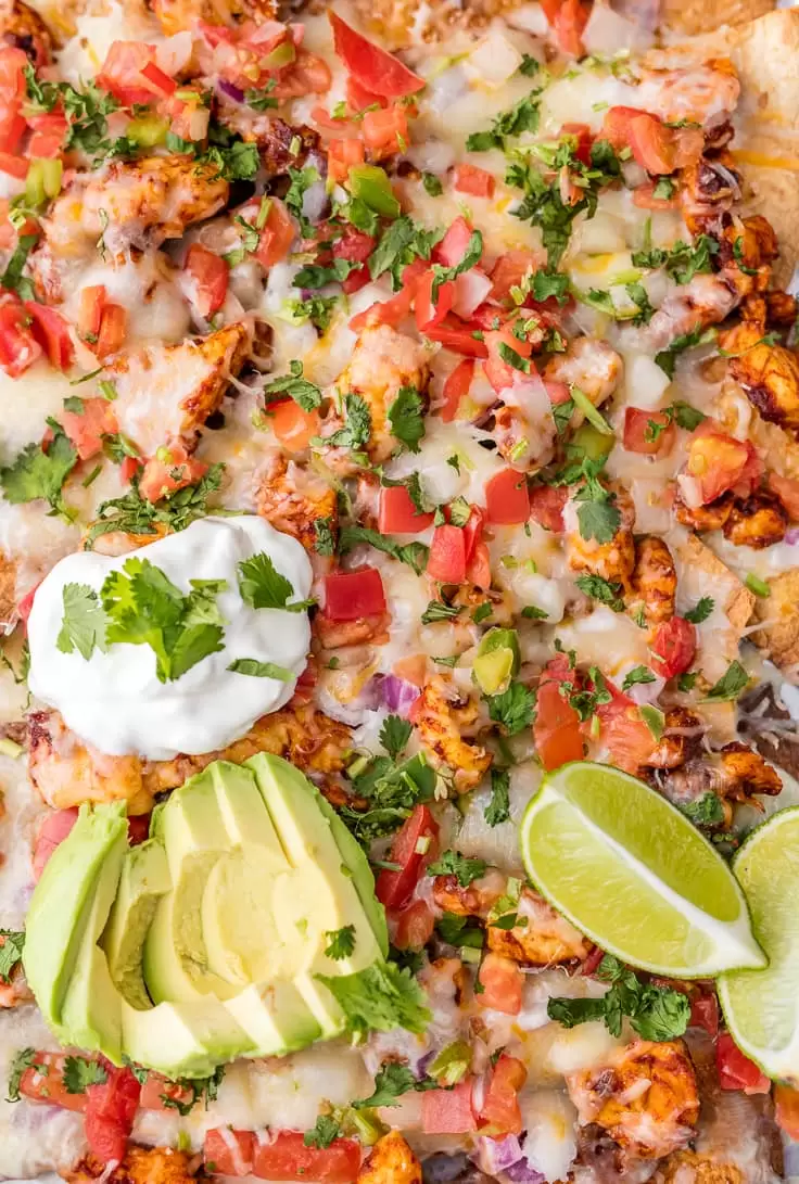 close up on chicken nachos topped with pico de gallo, sour cream, and avocado