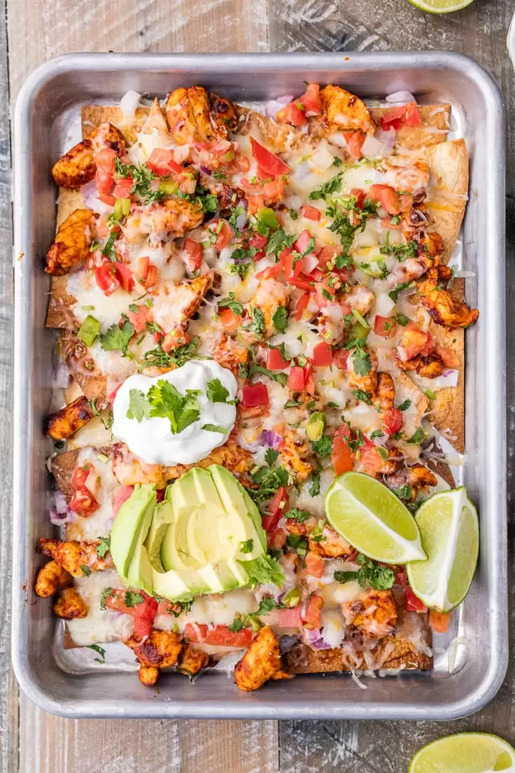 sheet pan nachos made with chicken, pico de gallo, onions, sour cream, avocado, lime, and more