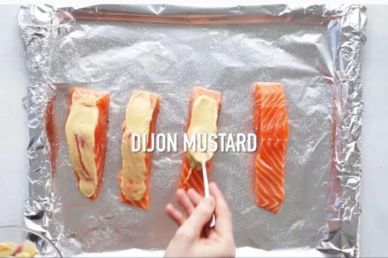 applying dijon mustard on salmon fillets in a baking sheet