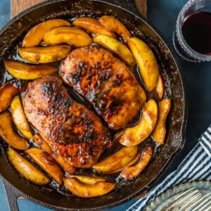 A cast iron skillet filled with pork chops and apples, accompanied by a glass of wine.