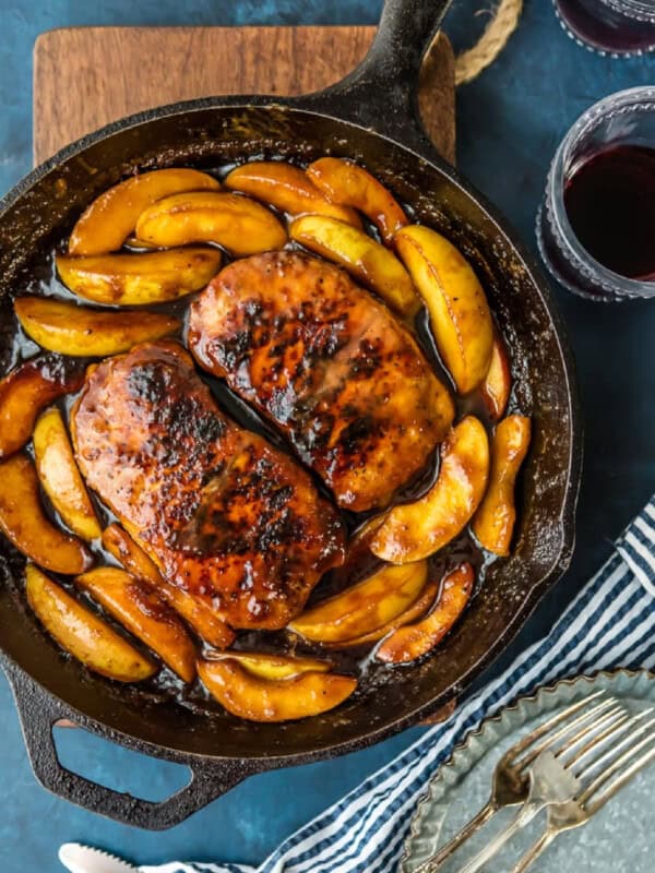 A cast iron skillet filled with pork chops and apples, accompanied by a glass of wine.