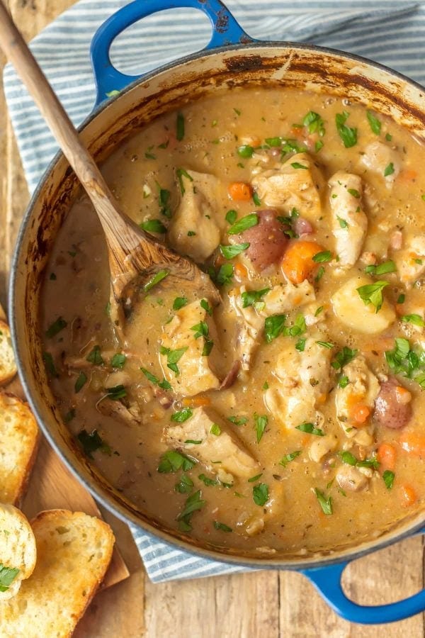 A hearty pot with chicken stew accompanied by bread and carrots.