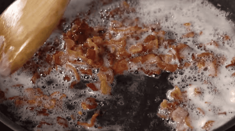 frying bacon pieces in a pan with a wooden spatula.