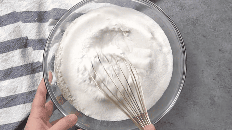 whisking flour, sugar, and other dry ingredients in a glass bowl.