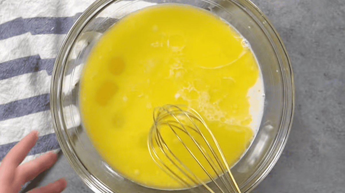 eggs, milk, and other wet ingredients in a glass bowl with a whisk.