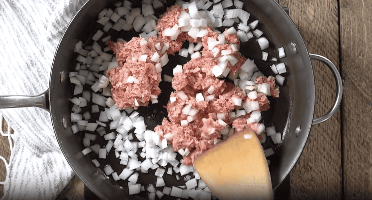 cooking ground sausage and diced onion in a pan with a wooden spoon.
