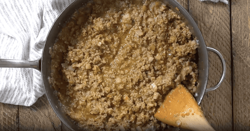 cooked seasoned sausage with salsa verde in a pan with a wooden spoon.