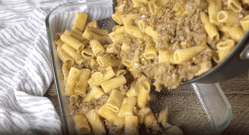 pouring sausage pasta into a baking dish.