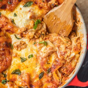 Lasagna cooked in a dutch oven with a wooden spoon.