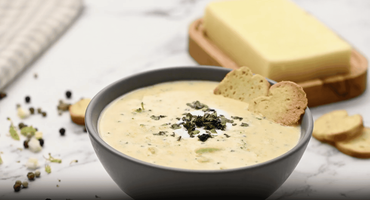 A closeup of a bowl of tomato soup with croutons, herbs, and parmesan cheese on top.