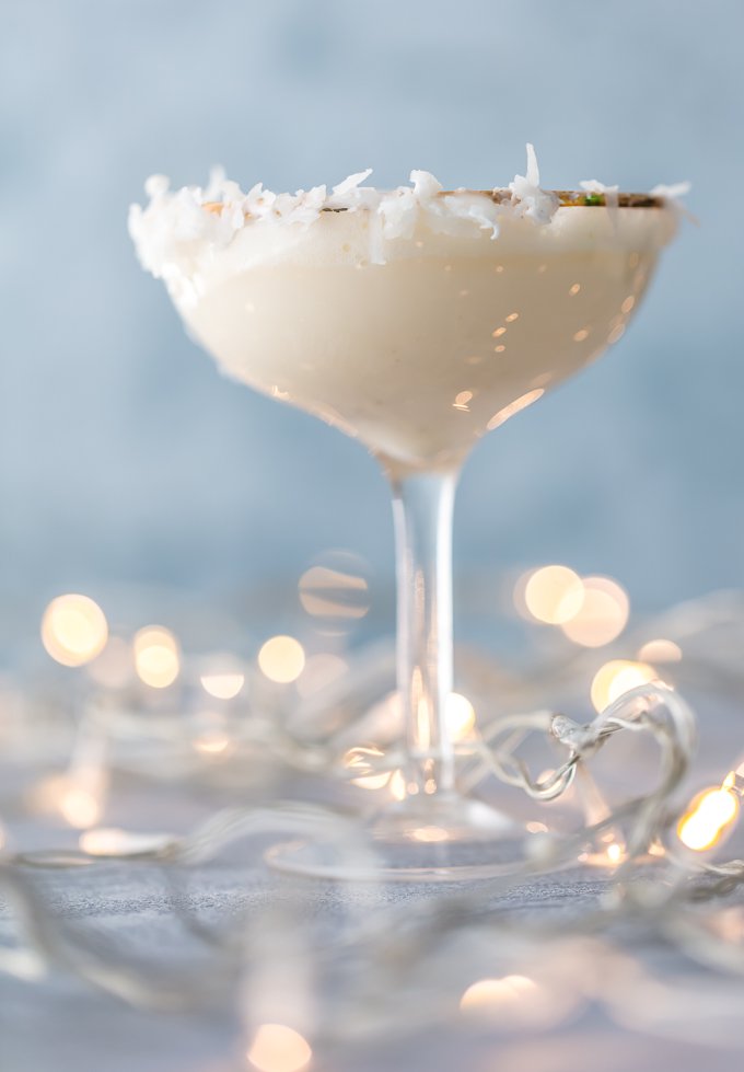 tall martini glass filled with festive holiday mocktail. Glass rim garnished with flaked coconut