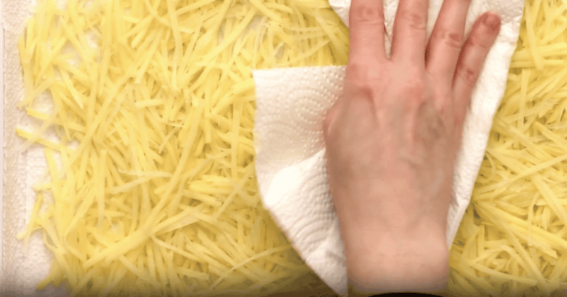 patting julienned potatoes dry on a paper towel-lined baking sheet.