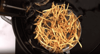 removing shoestring fries from hot oil with a mesh sieve.