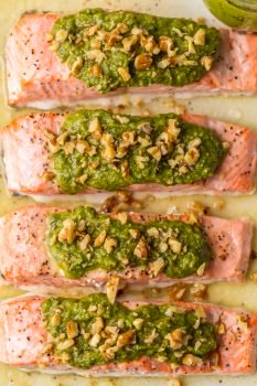 Baked Salmon with Basil Walnut Pesto is our favorite simple yet elegant seafood dinner. This Pesto Salmon Recipe is bursting with flavor and good fat. The tender flakey salmon is basted in butter, white wine, and lemon juice before baking and then topped with an amazing nutty and rich Basil Walnut Pesto. Best Salmon Recipe ever!