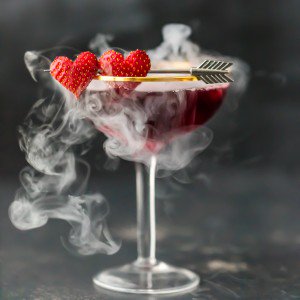 a cocktail with raspberries and arrows in the glass.