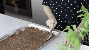 spreading chocolate over caramel saltines with an offset spatula.