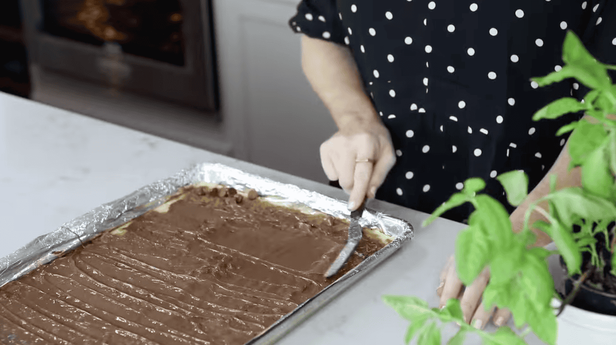 spreading chocolate over caramel saltines with an offset spatula.