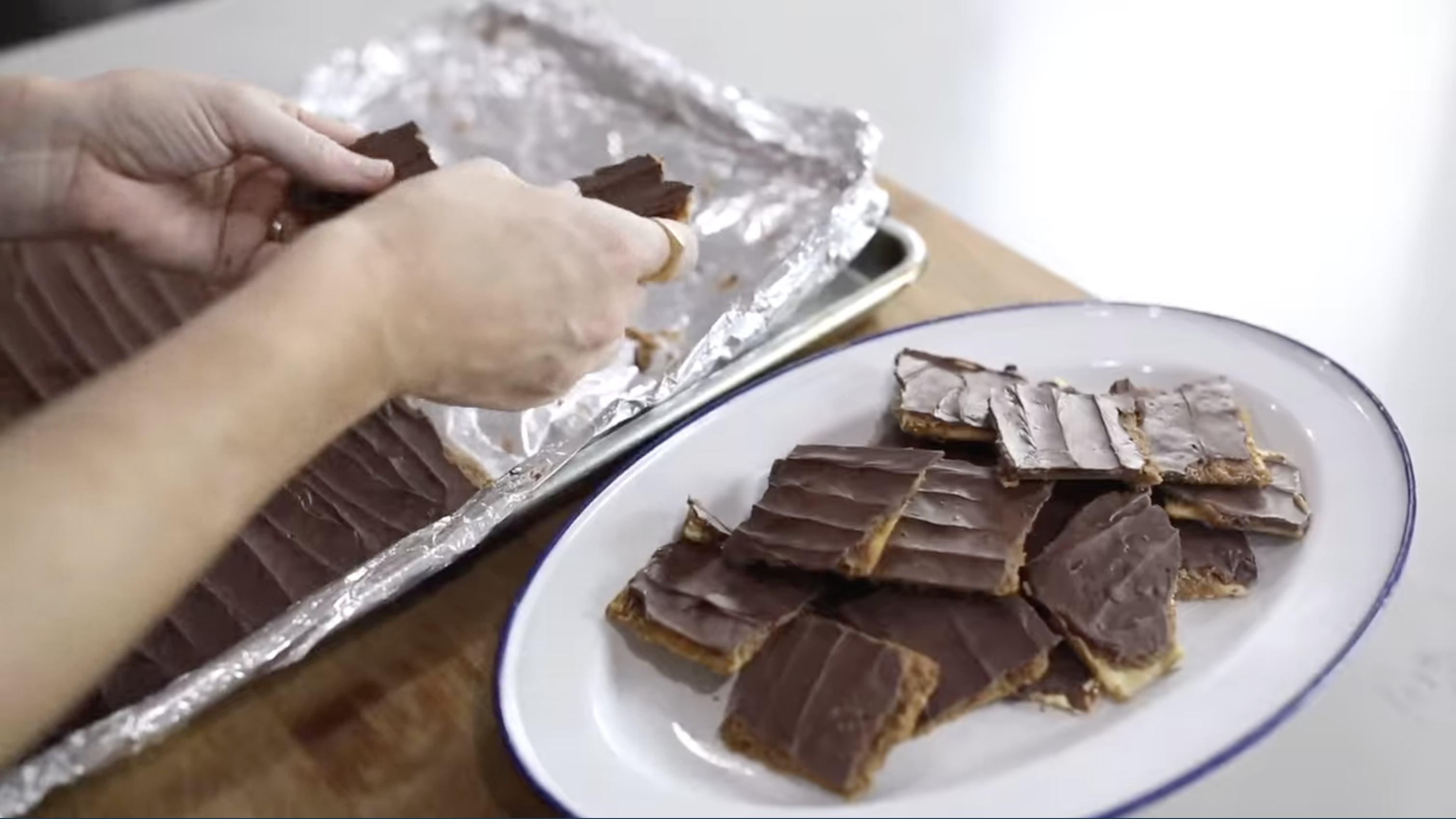 breaking saltine cracker toffee into pieces and placing them on a white tray.