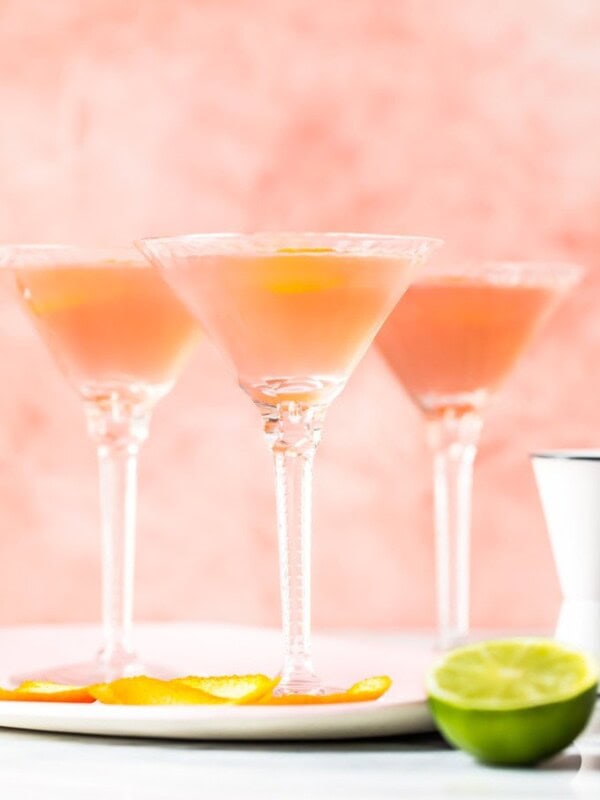 three glasses with cosmos inside beside a cut lime