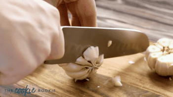 cutting the top off of a head of peeled garlic.