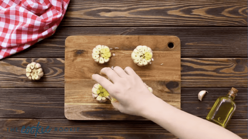 pouring olive oil over cut and peeled heads of garlic.