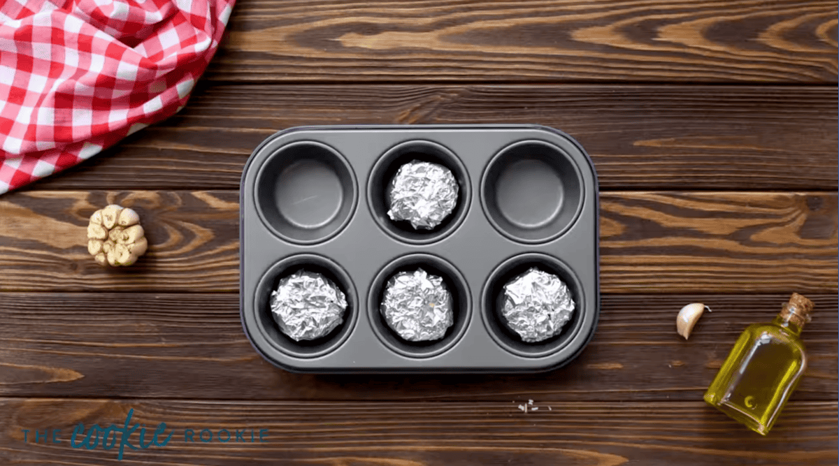 4 heads of garlic wrapped in aluminum foil in the wells of a muffin tin.