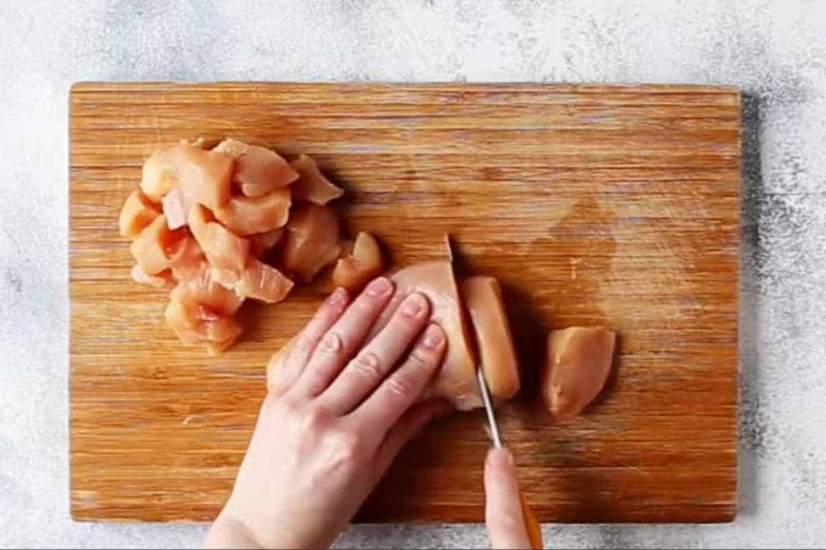 cutting the chicken breasts into bite size cubes with knife