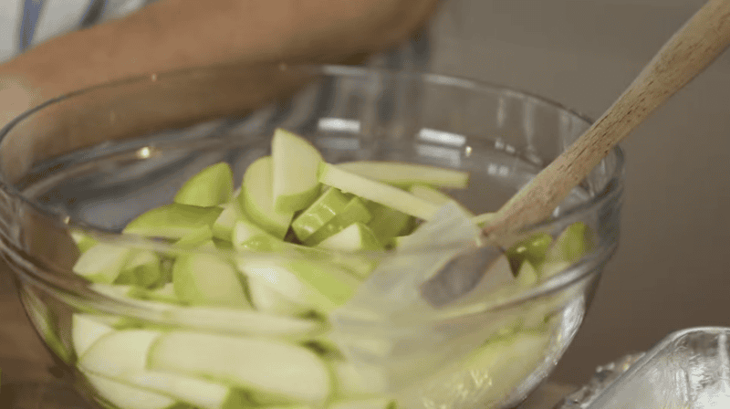 sliced apples in a glass bowl with a rubber spatula.