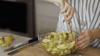 stirring spiced apple slices in a glass bowl with a rubber spatula.