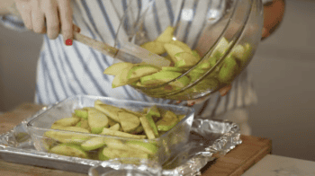 pouring spiced apple slices into a glass baking dish.