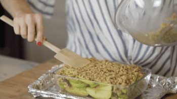 spreading crumble over apple slices in a glass baking dish.