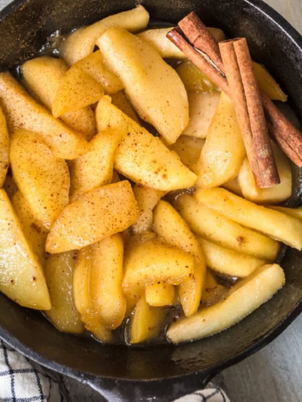 Fried sliced apples in a skillet with cinnamon sticks.