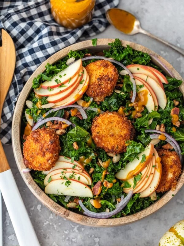 This Autumn Kale Salad recipe is the salad of the season! Made with kale, apples, onions, pumpkin seeds, bacon, fried goat cheese and a maple pumpkin salad dressing, it is the perfect fall salad idea. This delicious kale apple salad makes a tasty and healthy meal you'll want to eat all season long!