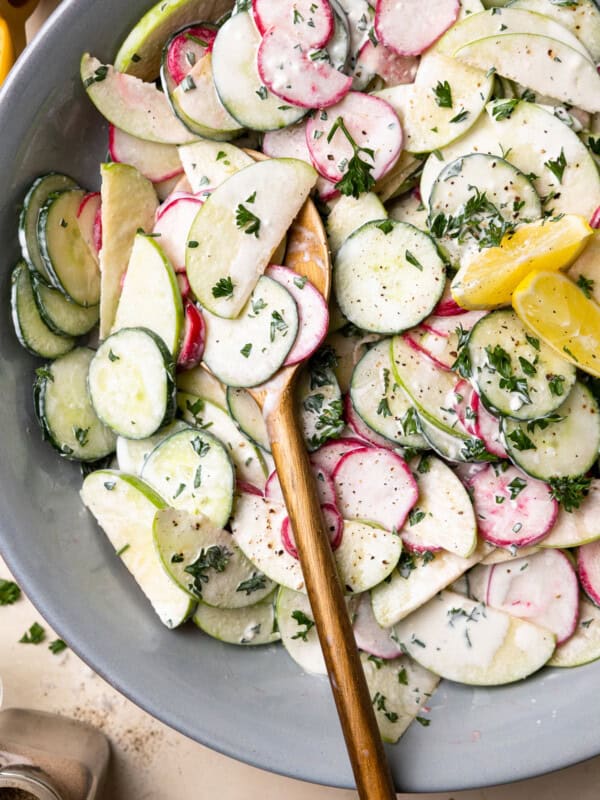 creamy cucumber salad in a gray serving bowl with wooden salad serving utensils.