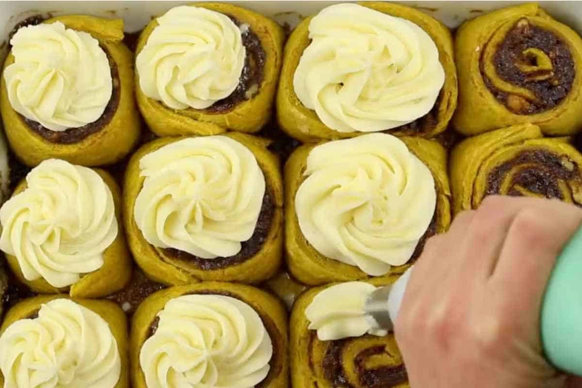 adding cream cheese frosting over room temperature pumpkin cinnamon rolls.