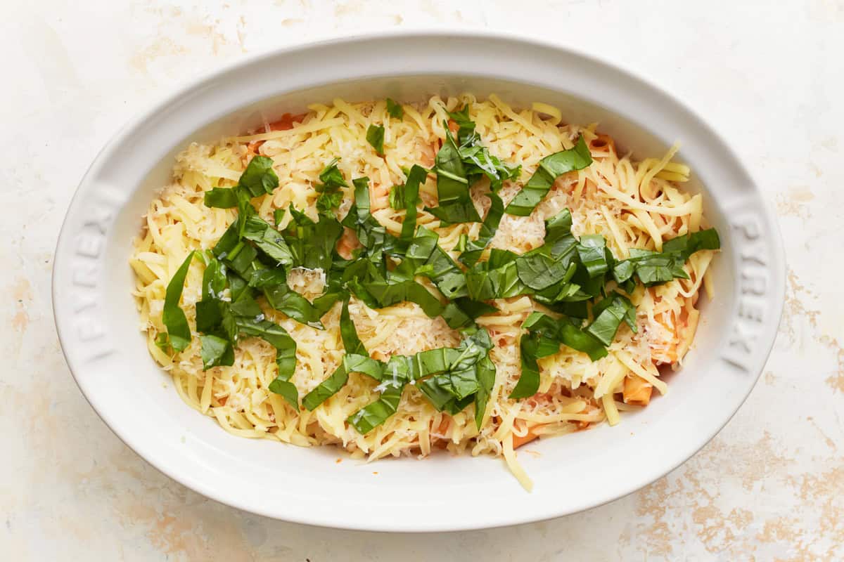 layers of cheese over creamy sauced noodles in an oval baking dish topped with basil.