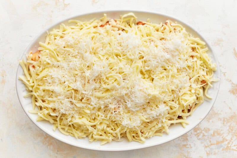 layered baked ziti in an oval baking dish topped with cheese.