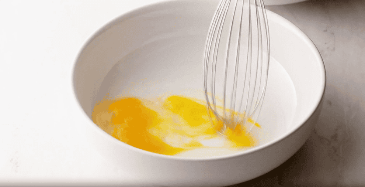 whisking an egg in a shallow white bowl.