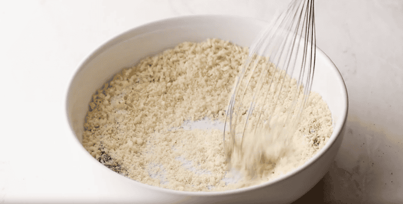 whisking seasoned breadcrumbs in a shallow white bowl.